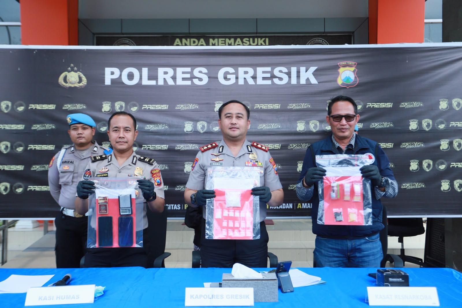 GRESIK - Satresnarkoba Polres Gresik Polda Jatim kembali menunjukkan komitmennya dalam memberantas peredaran narkotika. Kali ini, Dua pria berinisial DE (32) dan MWF (30) berhasil ditangkap bersama barang bukti sabu seberat total 38,066 gram yang diduga siap diedarkan di wilayah Gresik selatan. Kapolres Gresik AKBP Ramadhan Nasution menegaskan bahwa pengungkapan kasus tersebut merupakan bukti keseriusan Polres Gresik Polda Jatim dalam memutus mata rantai peredaran narkoba di wilayah hukumnya. "Kasus ini terungkap setelah Polisi menerima informasi masyarakat mengenai maraknya peredaran narkoba di kawasan Gresik selatan," ujar AKBP Ramadhan, Jumat (24/7/2026). Polres Gresik Bongkar Peredaran Narkoba Sistem Ranjau, Dua Kurir Sabu Diamankan Menindaklanjuti informasi tersebut, Tim Opsnal Satresnarkoba kemudian melakukan penyelidikan hingga menggerebek sebuah rumah kos di Desa Pasinan Lemahputih, Kecamatan Wringinanom, pada Minggu (19/7/2026). Dari lokasi tersebut, Polisi mengamankan kedua tersangka beserta 17 paket sabu yang telah dipecah untuk diedarkan sesuai pesanan. Selain sabu, Polisi turut menyita timbangan digital, alat hisap, plastik klip, dua telepon seluler, serta satu unit sepeda motor yang digunakan pelaku. "Nilai ekonomis sabu yang disita diperkirakan mencapai Rp68,4 juta," ujar AKBP Ramadhan. Dari hasil pemeriksaan, terungkap kedua tersangka berperan sebagai kurir dengan modus sistem ranjau, yakni meletakkan paket sabu di titik-titik tertentu untuk kemudian diambil pembeli. "Kedua tersangka diketahui telah menjalankan aktivitas tersebut selama sekitar empat bulan dengan wilayah edar meliputi Wringinanom, Driyorejo, Karangandong hingga Legundi," terang AKBP Ramadhan. Selain sabu, Polisi turut menyita timbangan digital, alat hisap, plastik klip, dua telepon seluler, serta satu unit sepeda motor yang digunakan pelaku. "Nilai ekonomis sabu yang disita diperkirakan mencapai Rp68,4 juta," ujar AKBP Ramadhan Dalam sepekan, keduanya mampu mengedarkan sekitar 40 gram sabu dan memperoleh upah Rp25 ribu untuk setiap titik ranjau yang dipasang. Kapolres Gresik menambahkan, pihaknya masih terus melakukan pengembangan guna mengungkap pemasok utama yang kini telah masuk daftar pencarian orang (DPO). "Kami mengajak masyarakat untuk tidak ragu melaporkan apabila mengetahui adanya penyalahgunaan maupun peredaran narkoba, melaporkan melalui Call Centre 110 dan selain itu Masyarakat juga bisa menghubungi melalui Hotline khusus ‘Lapor Cak Rama’ di nomor 0811-8800-2006," ujar AKBP Ramadhan Nasution. Atas perbuatannya, kedua tersangka dijerat Pasal 114 ayat (2) jo Pasal 132 ayat (1) Undang-Undang Nomor 35 Tahun 2009 tentang Narkotika sebagaimana telah disesuaikan, dipidana dengan pidana mati, pidana penjara seumur hidup, atau pidana penjara paling lama 20 (dua puluh) tahun.